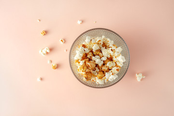 Popcorn in a glass bucket on pink colored background, top view