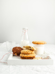 Selection of homemade cookies, milk, winter decor on wooden tray on white background