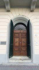 Old Tuscan dark wooden door with green shutters in a white neoclassical style building