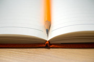 A pencil between pages of the daybook on the wooden background. Concept photo.