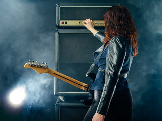 Woman guitarist turning knobs on amplifier