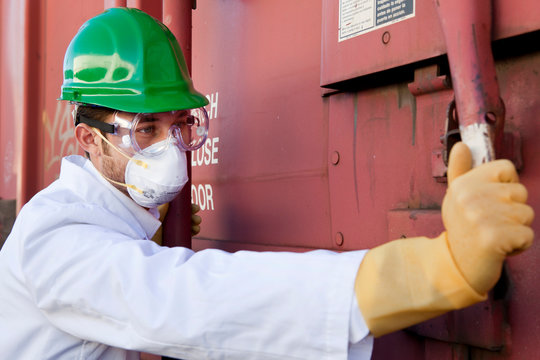 Worker In Hazmat Suit, Hard-hat And Face Mask Closing Metal Door