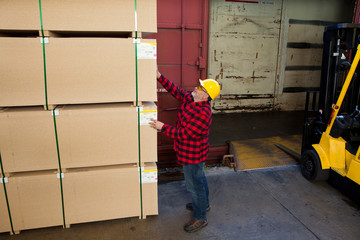 Worker inspecting wood pallet standing by fork lift truck
