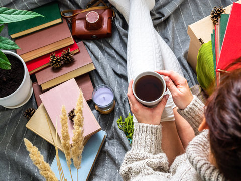 A girl in a knitted sweater drinking tea surrounded by books