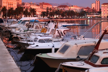 Small fishing boats and historic buildings on Riva promenade in Split, Croatia illuminated by pink sunset light. Selective focus.