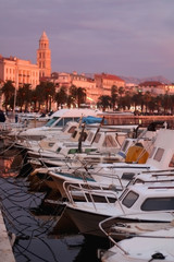 Small fishing boats and historic buildings on Riva promenade in Split, Croatia illuminated by pink sunset light. Selective focus.