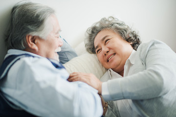 Obraz premium Senior Asian couple love lying on the bed with hug and hold the hand. Retired man and woman sleeping with talking on bed in bed room at home which smiling and felling happy. Old couple love concept