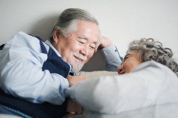 Senior Asian couple love lying on the bed with hug and hold the hand. Retired man and woman sleeping with talking on bed in bed room at home which smiling and felling happy. Old couple love concept