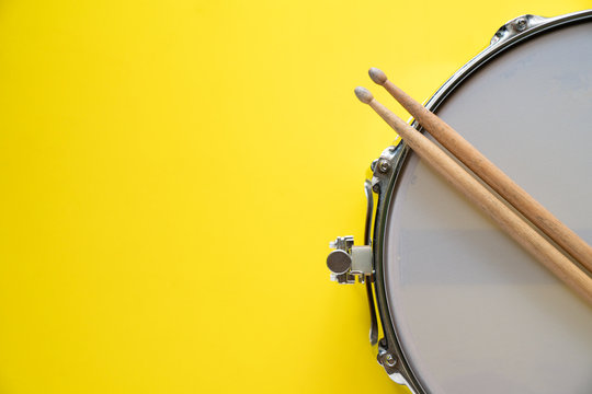 Drum stick and drum on yellow table background, top view, music concept