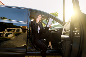 Serious young business woman dressed in formal wear talking with partner via mobile phone and using...