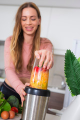 Woman blending smoothie with blender in the kitchen
