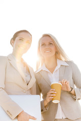 Young businesswomen with disposable cup and laptop looking away against sky
