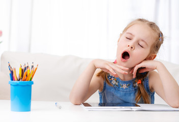Little girl yawning when making her homework with digital tablet