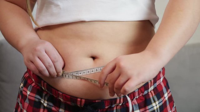 Overweight, fat girl measuring her stomach, close-up shot