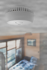 Domestic smoke alarm / battery powered smoke detector on the ceiling in room filled with smoke from...
