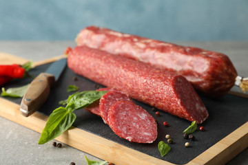 Cutting board with sausage, spice and knife on grey background, close up