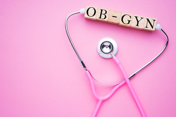 Women in healthcare concept. A pink strethoscope on a pink background, with wooden block spelling OB-GYN, or Obstetrics and Gynaecology