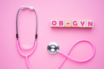 Women in healthcare concept. A pink strethoscope on a pink background, with wooden block spelling OB-GYN, or Obstetrics and Gynaecology