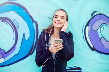 Female jogger listening music on mobile phone in front of graffiti wall