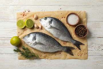 Baking paper with Dorado fishes and cooking ingredients on wooden background, top view
