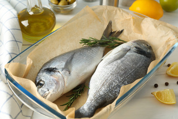 Baking tray with Dorado fishes and cooking ingredients on wood background, close up