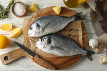 Board with Dorado fishes and cooking ingredients on wooden background, top view