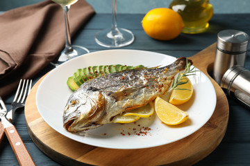 Plate with baked Dorado fish on garnished wooden background, close up