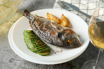 Plate with baked Dorado on garnished grey background, close up