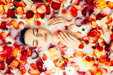 Young girl relaxes in a bath with rose petals, top view. Spa treatments