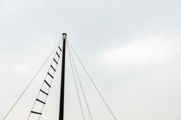 Obraz premium top of small ship masts in sky cloud background copy space with rope ladder used to observe.