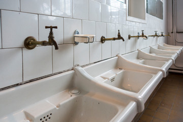 Row of dirty white sinks / wash basins in bathroom of disused clinic
