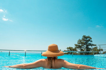 Fototapeta na wymiar Blonde woman in straw hat in swimming pool with blue endless sky background 