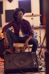 Fototapeta na wymiar Full length portrait of contemporary African man looking away pensively while posing in music recording studio