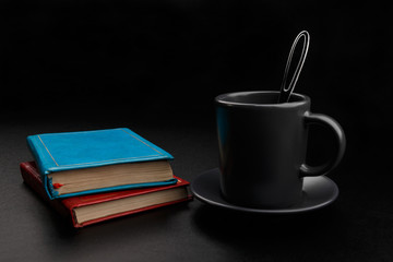 Cup of coffee with spoon and books on black background