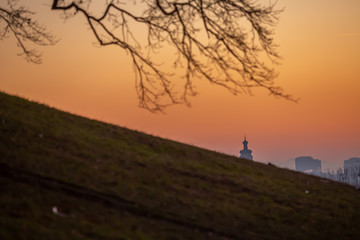 Tree silhouette, a church top dome and cross in this beautiful colorful cold winter sunset in the city park.