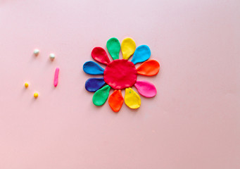 Obraz na płótnie Canvas cute flower made of multi-colored plasticine clay on a pink background, multi-colored dough, minimal, children's crafts