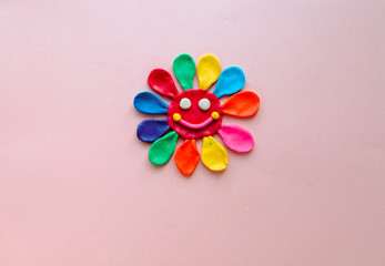 cute flower made of multi-colored plasticine clay on a pink background, multi-colored dough, minimal, children's crafts