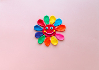 cute flower made of multi-colored plasticine clay on a pink background, multi-colored dough, minimal, children's crafts