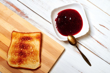 Toasted toast on a plate and jam on a light wooden background.
