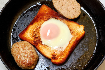 Toast with an egg and a patty in a pan.