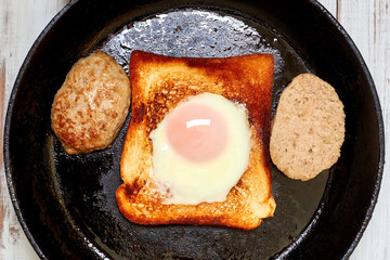 Toast with an egg and a patty in a pan.