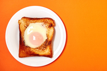 Toast with an egg on a plate on a orange background.