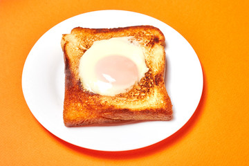 Toast with an egg on a plate on a orange background.