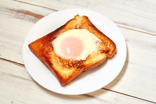 Toast with an egg on a plate on a light wooden background.