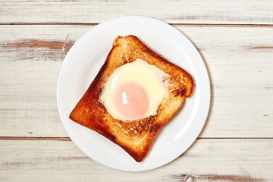 Toast with an egg on a plate on a light wooden background.