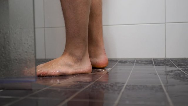 Man feet entering in the shower cabin - skin care at home. Close-up of man wet legs and feet in the shower. Traking from right to left