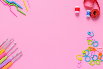 Colorful crocheting and knitting accessories on soft pink background with copy space