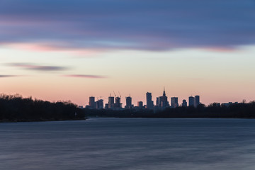 Warsaw skyline with skyscrapers during colorful sunset over the Vistula River.