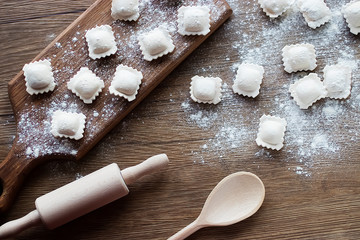 Uncooked ravioli with meat on a brown wooden board. The process of cooking homemade ravioli.