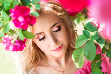 Obraz na płótnie Canvas beautiful portrait of a blonde girl in pink roses. close-up, makeup, extended eyelashes